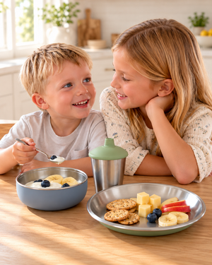 Two kids at the kitchen table with Monkey Proof stainless steel kids bowl, plate and sippy cup
